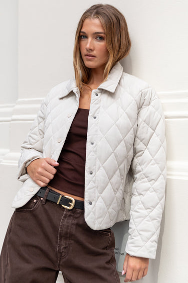 Woman wearing a white quilted jacket against a white wall