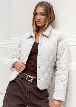 Woman wearing a white quilted jacket against a white wall