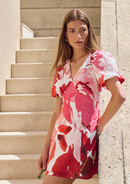 Woman in a red and white floral dress standing on stone steps with greenery in the background