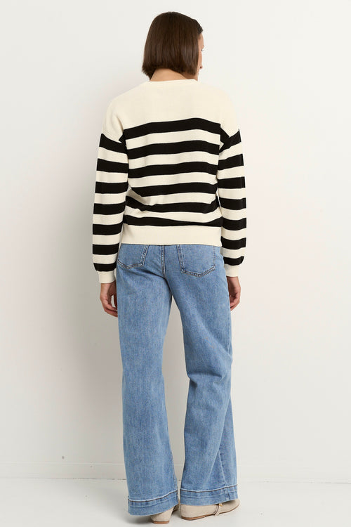 Woman wearing a black and ivory striped crew neck sweater with full-length sleeves, styled casually with light blue wide-leg jeans.