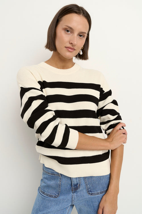 Woman wearing a black and ivory striped crew neck sweater with full-length sleeves, styled casually with light blue wide-leg jeans.
