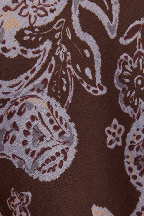 A close-up of a brown fabric with a detailed paisley and floral pattern in beige, white, and dark brown.