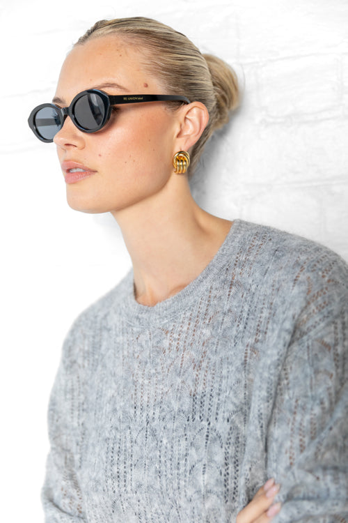 Woman wearing sunglasses and a gray sweater against a white background