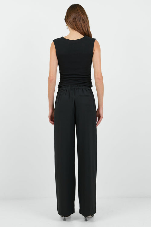 Woman wearing a black sleeveless top and wide-leg pants on a white background