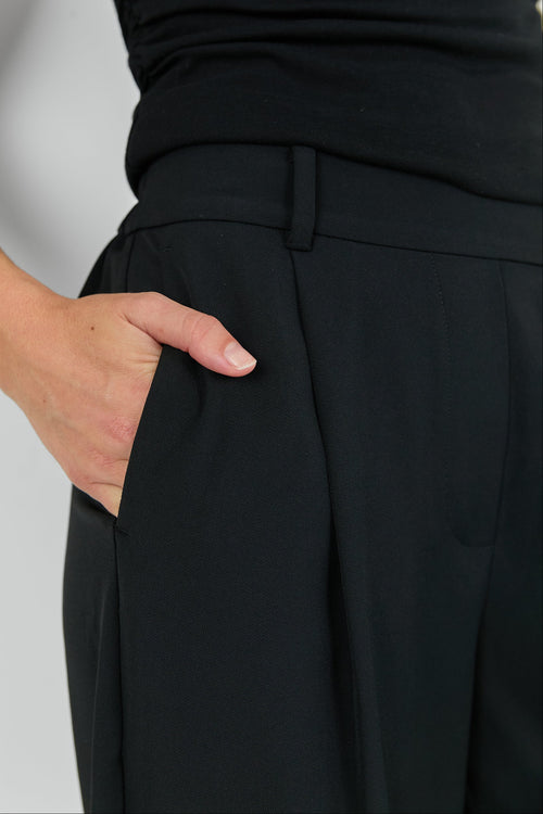 Person wearing a black outfit with a belt on a light gray background