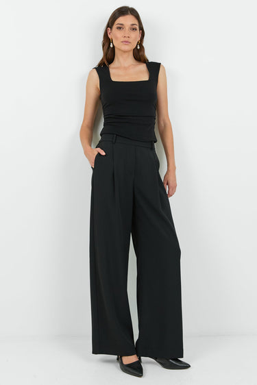 Woman wearing a black sleeveless top and wide-leg pants on a white background