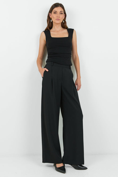 Woman wearing a black sleeveless top and wide-leg pants on a white background