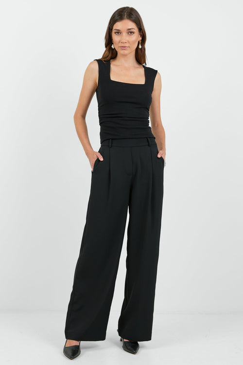 Woman wearing a black sleeveless top and wide-leg pants on a white background