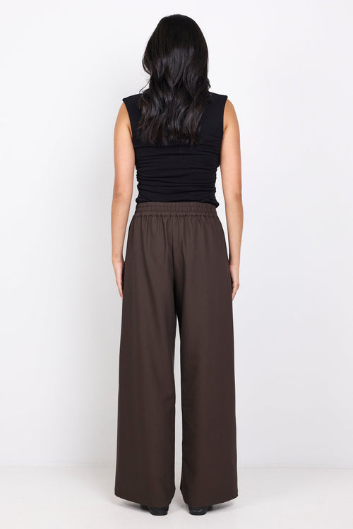Woman wearing a black sleeveless top and brown wide-leg pants on a white background
