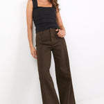 Woman wearing a black sleeveless top and brown high-waisted pants on a white background