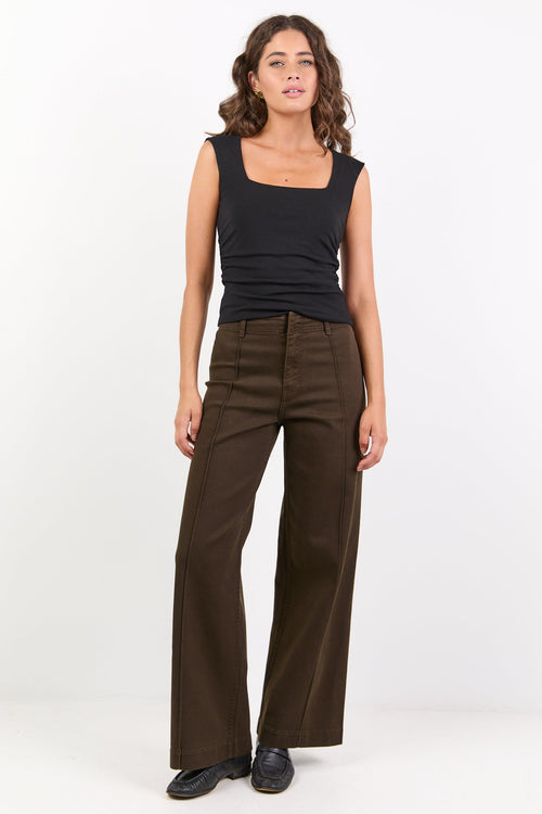 Woman wearing a black sleeveless top and brown high-waisted pants on a white background