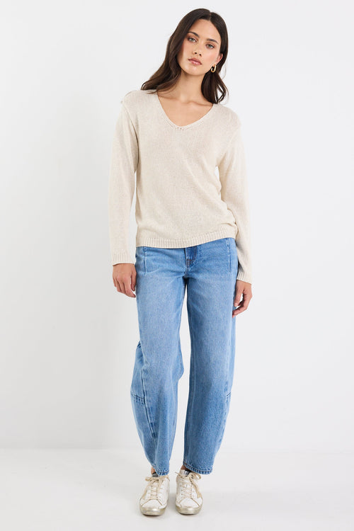 Woman wearing a beige sweater and blue jeans on a white background