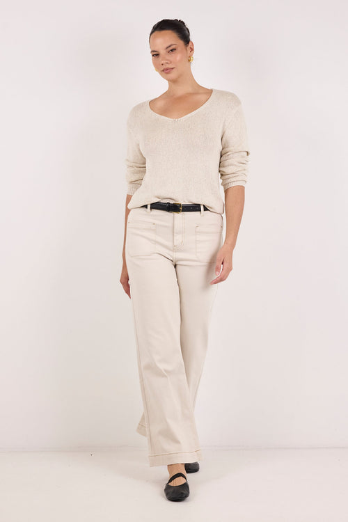 A woman modeling a cream-colored knit long-sleeve top and matching cream wide-leg trousers, styled with a thin black belt and black flats, against a plain white studio background.