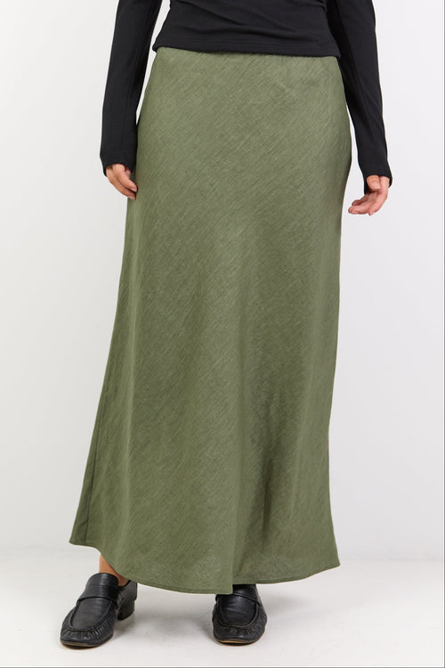 Person wearing a black long-sleeve top and green skirt on a white background