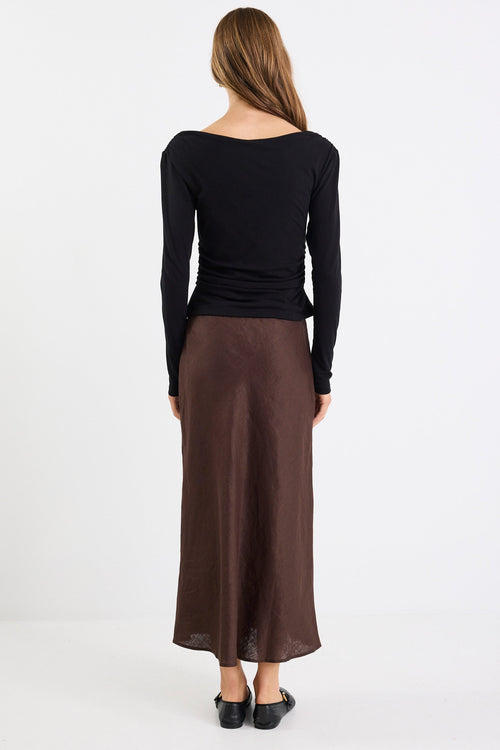 Person wearing a black long-sleeve top and brown skirt on a white background