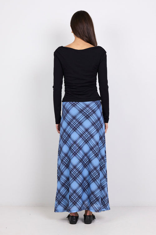 Person wearing a black long-sleeve top and blue plaid skirt on a white background