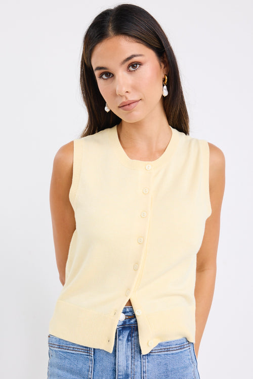 Woman wearing a sleeveless yellow vest with button-down front and crew neck, paired with blue jeans.