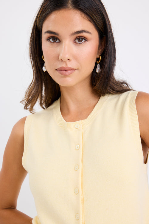 Woman wearing a sleeveless yellow vest with button-down front and crew neck, paired with blue jeans.