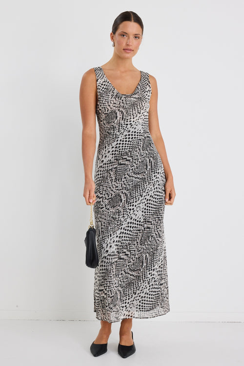 Woman wearing a sleeveless, bias-cut midi dress with a charcoal snake print, styled with black heels against a white wall.