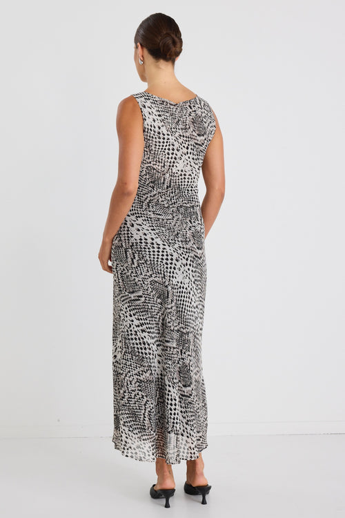 Woman wearing a sleeveless, bias-cut midi dress with a charcoal snake print, styled with black heels against a white wall.