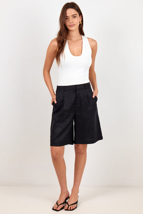 A woman modeling a white sleeveless tank top and black wide-leg shorts against a plain white studio background.