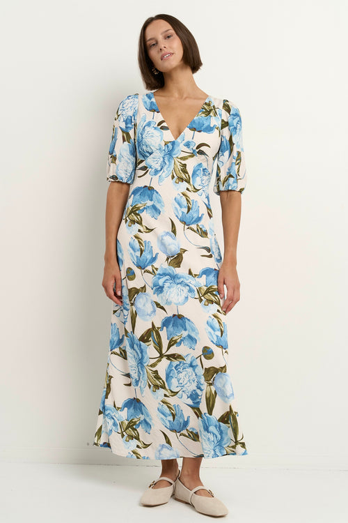 Woman wearing a short sleeve floral midi dress with a V-neck and blue rose print on a cream base.