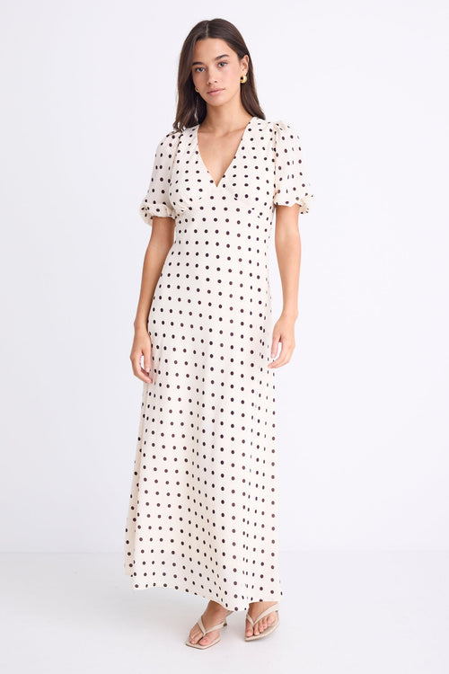 Woman wearing a cream midi dress with chocolate polka dots, V-neckline, short puff sleeves, and a flattering bias-cut silhouette.