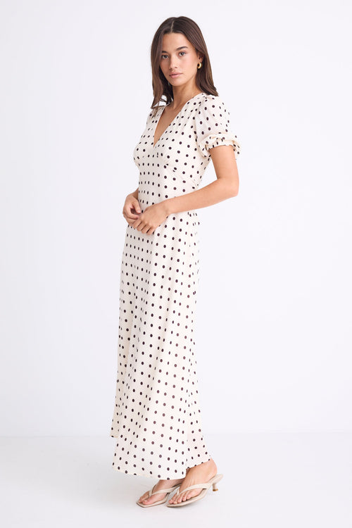 Woman wearing a cream midi dress with chocolate polka dots, V-neckline, short puff sleeves, and a flattering bias-cut silhouette.