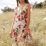 Woman in a floral dress standing in a grassy field with trees and blue sky in the background