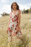 Woman in a floral dress standing in a grassy field with trees and blue sky in the background