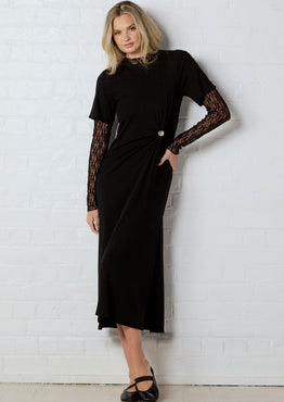 Woman wearing a black dress with lace sleeves against a white wall