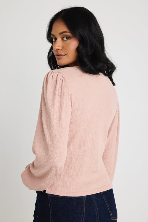 Model wears a blush pink top with jeas