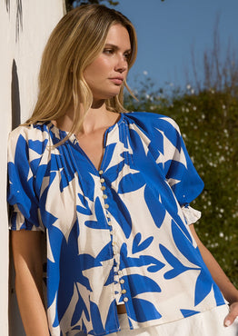 Woman wearing a blue and white floral blouse standing outdoors.