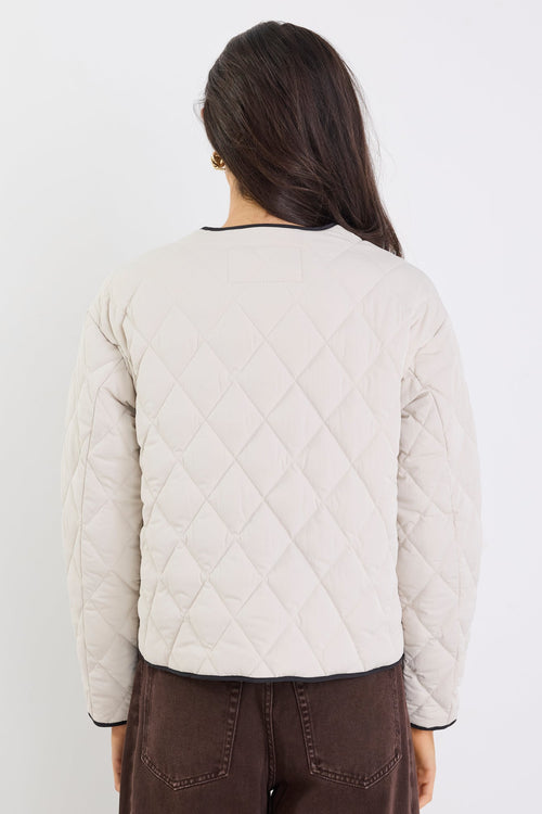 Person wearing a light-colored quilted jacket and brown pants on a white background