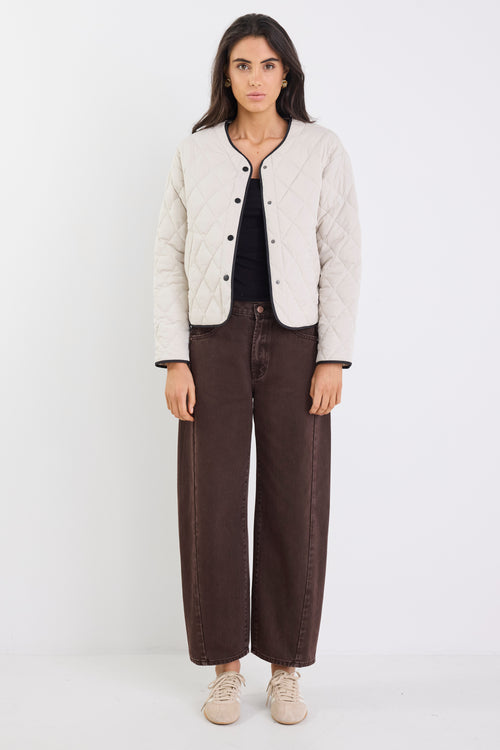 Woman wearing a beige quilted jacket, black top, and brown wide-leg jeans on a white background