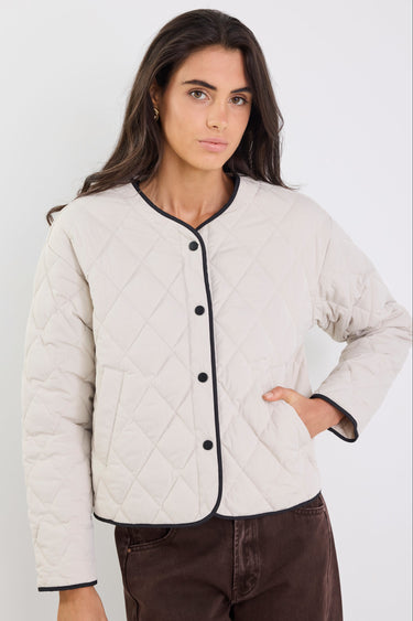 Woman wearing a beige quilted jacket with black buttons against a white background