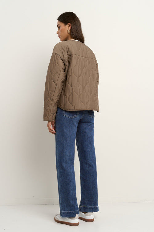 Woman wearing an oversized quilted mocha colored jacket with button front, styled with blue jeans and gold hoop earrings.
