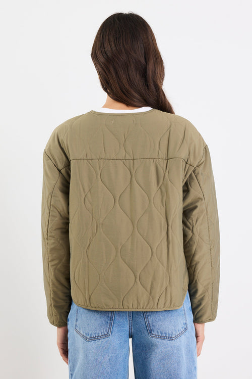 Person wearing a green quilted jacket and blue jeans on a white background