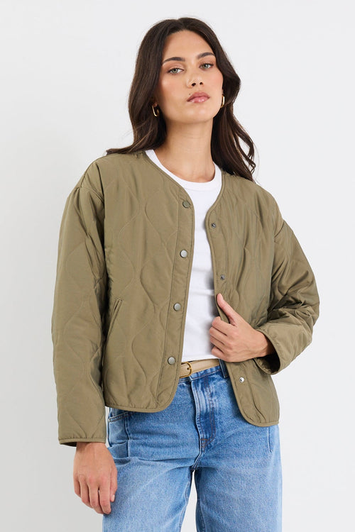 Woman wearing a green jacket, white shirt, blue jeans, and beige sneakers on a white background