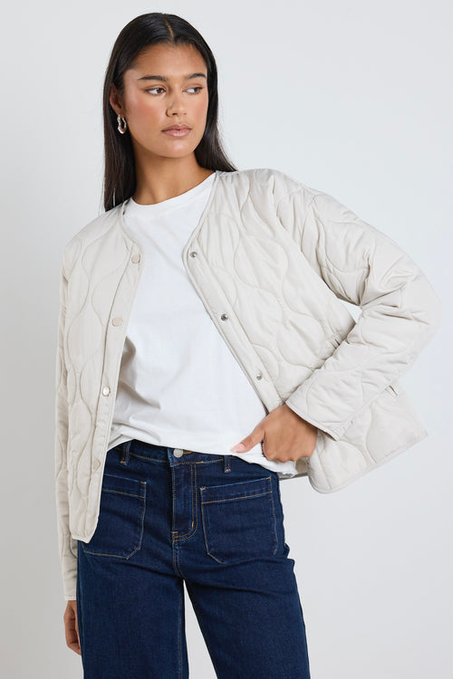  A quilted putty puffer jacket styled with a white tee and indigo denim, creating a relaxed yet elevated everyday look.