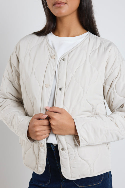  A quilted putty puffer jacket styled with a white tee and indigo denim, creating a relaxed yet elevated everyday look.