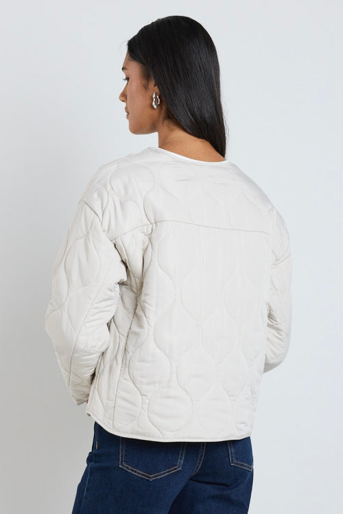  A quilted putty puffer jacket styled with a white tee and indigo denim, creating a relaxed yet elevated everyday look.