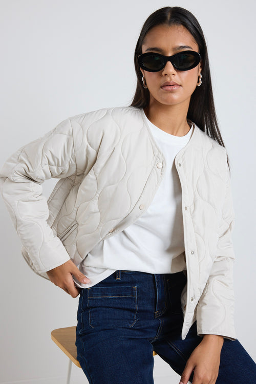  A quilted putty puffer jacket styled with a white tee and indigo denim, creating a relaxed yet elevated everyday look.