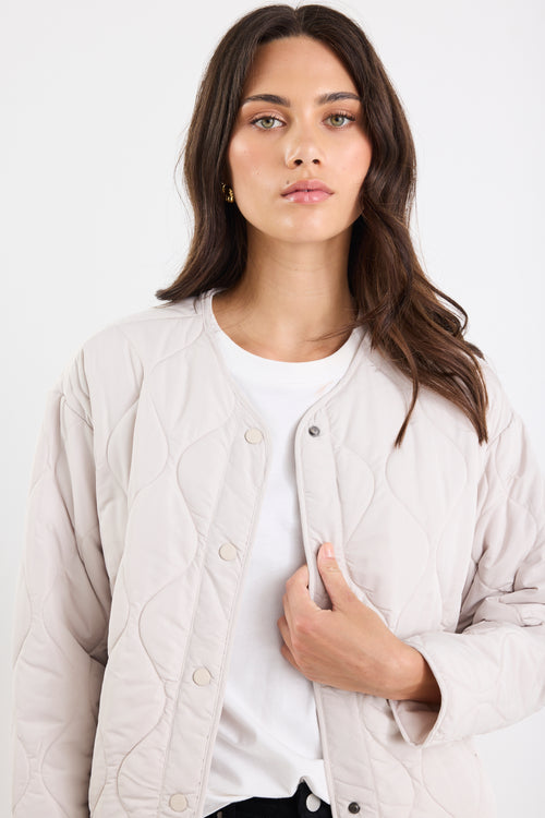 Woman wearing a light beige quilted jacket over a white shirt on a white background