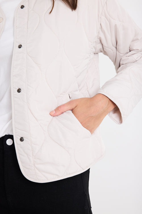 Person wearing a white quilted jacket with a neutral background