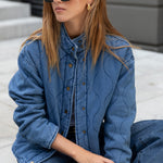 Woman wearing a blue denim jacket and sunglasses sitting on steps.