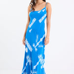 Woman wearing a bright blue strappy bias-cut slip midi dress with white palm and geometric print, relaxed fit, and fluid drape.