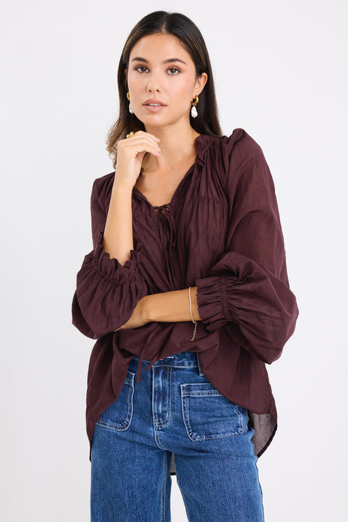 model wears a brown long sleeve blouse with blue jeans