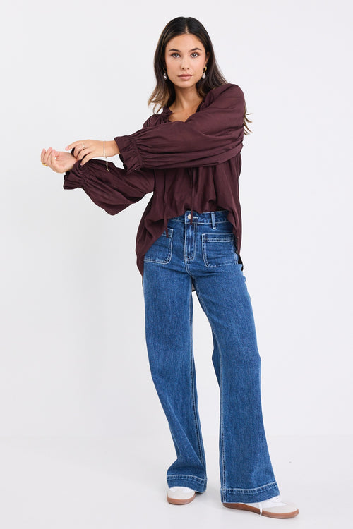 model wears a brown long sleeve blouse with blue jeans