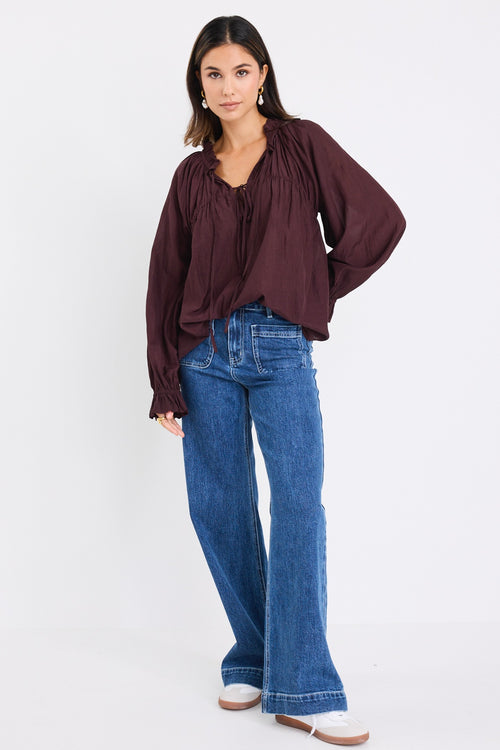 model wears a brown long sleeve blouse with blue jeans
